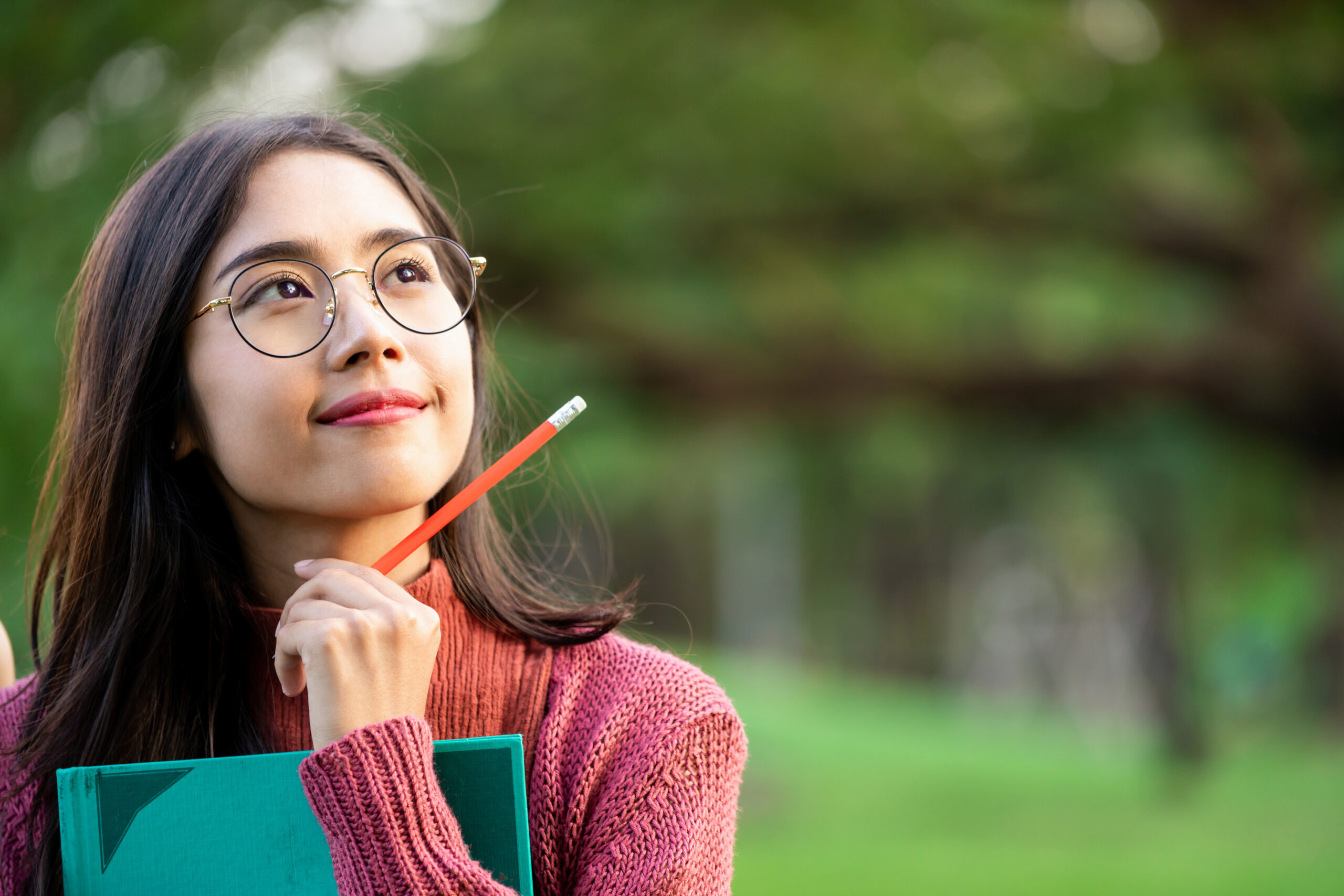 Young creative student girl thinking or planning future education while holding pencil in hand. Creativity idea and learning concept.